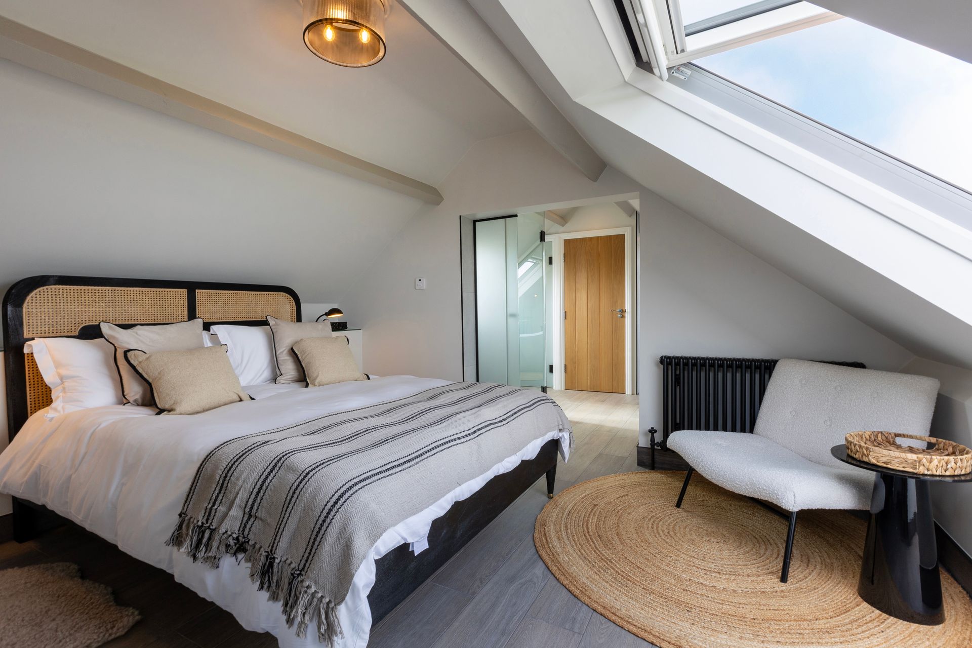 A bedroom with a bed , chair , table and skylight.