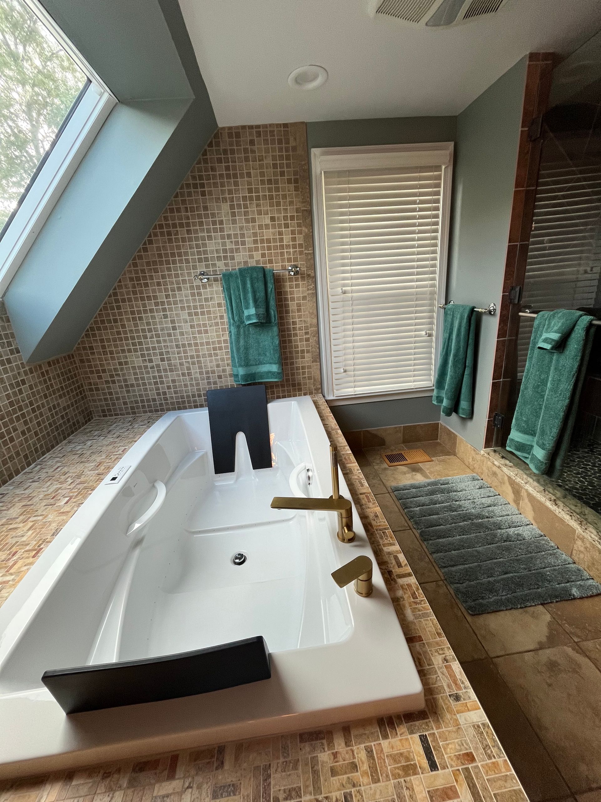 Bathroom with a jacuzzi tub, brick wall, blinds, and teal towels.