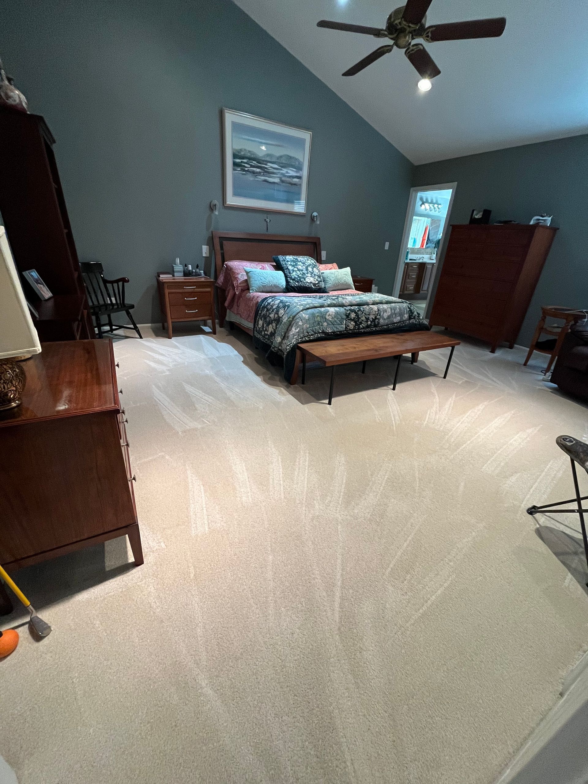 Bedroom with vaulted ceiling, bed, furniture, and light-colored carpet. Teal walls and a ceiling fan.