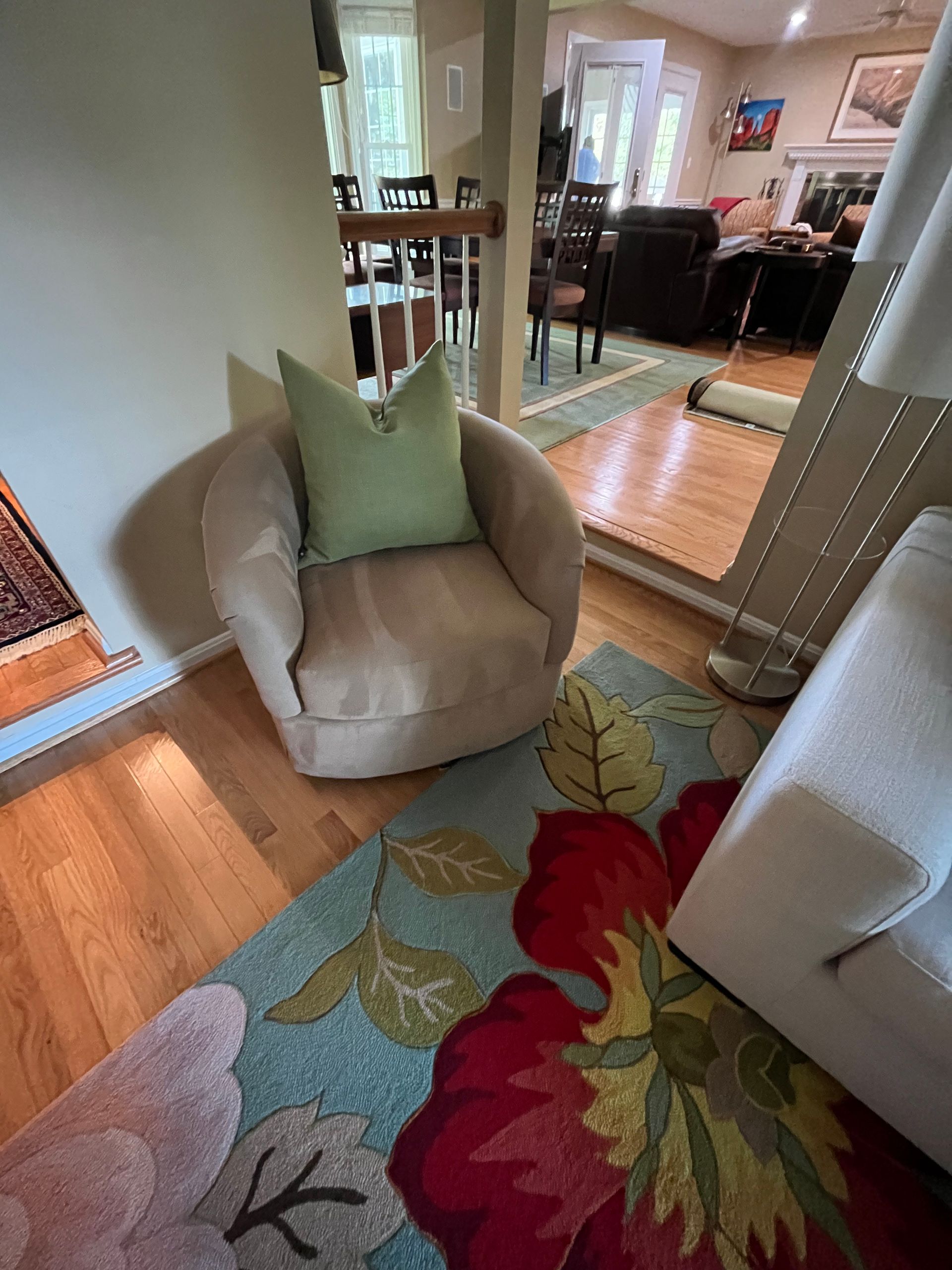 Tan swivel chair with green pillow on floral rug, hardwood floors, looking into another room.