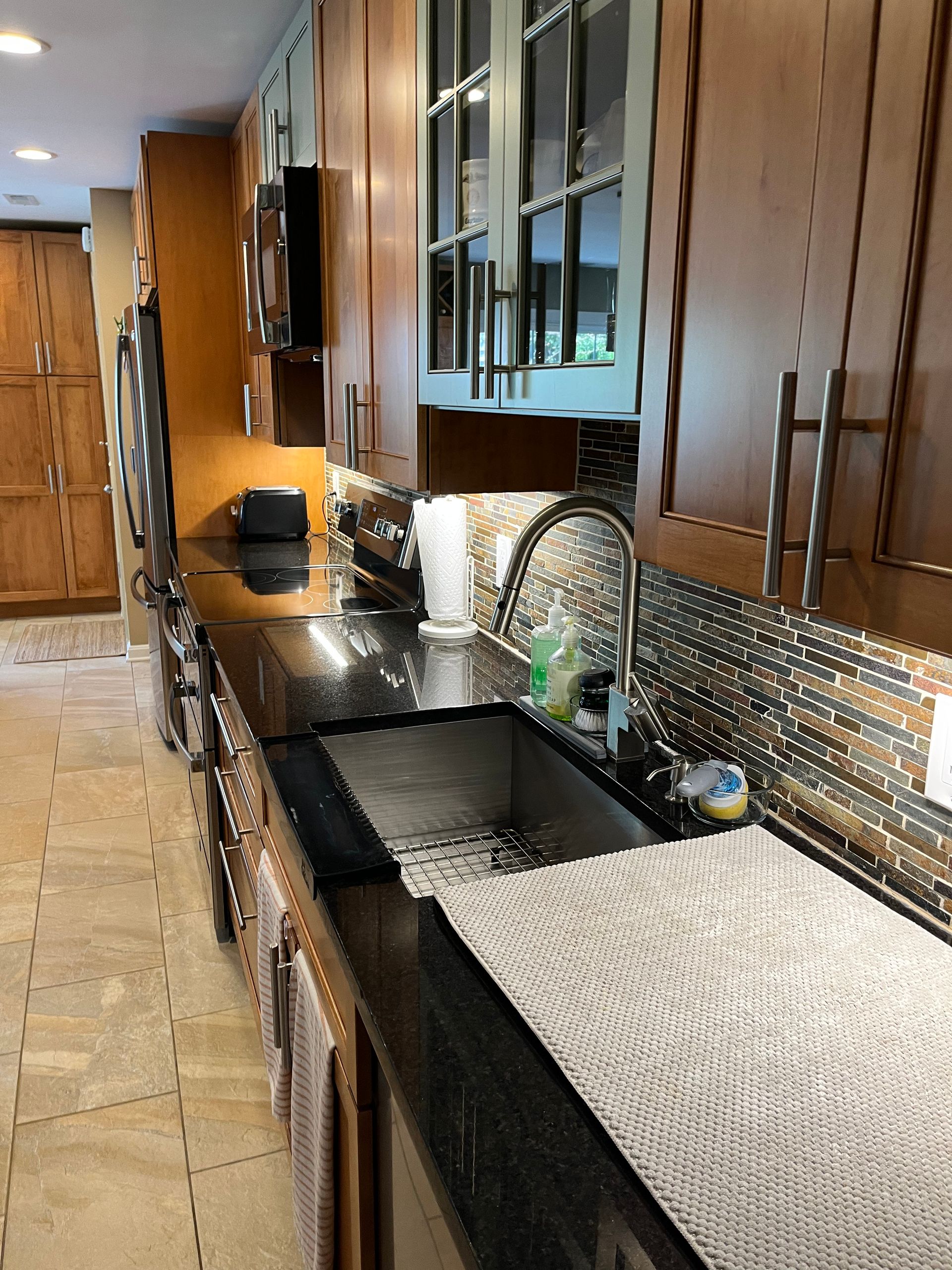 Kitchen with dark countertops, stainless steel sink and appliances, and light brown cabinetry.