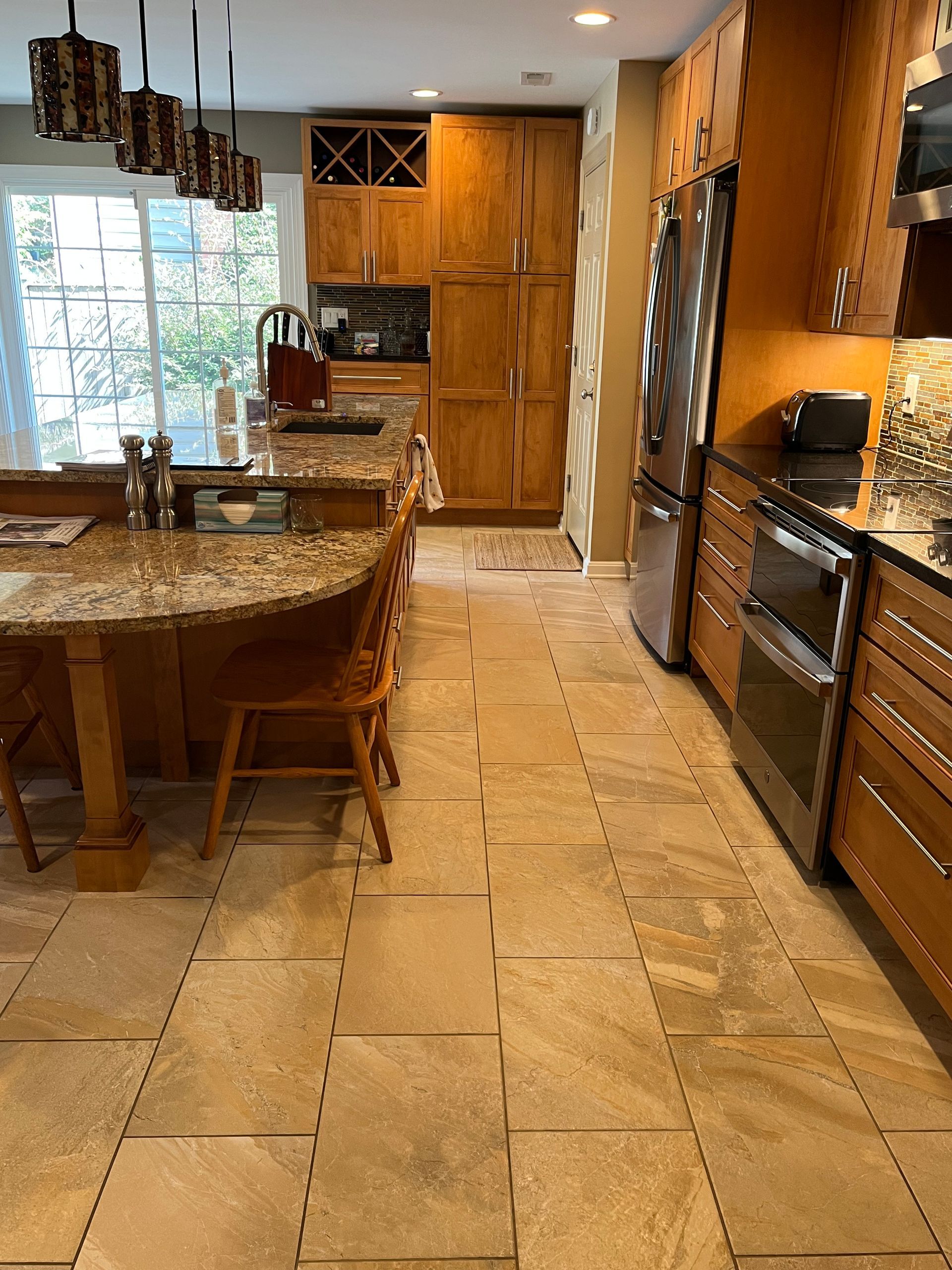 Kitchen with wood cabinets, island with seating, stainless steel appliances, and tile floor.