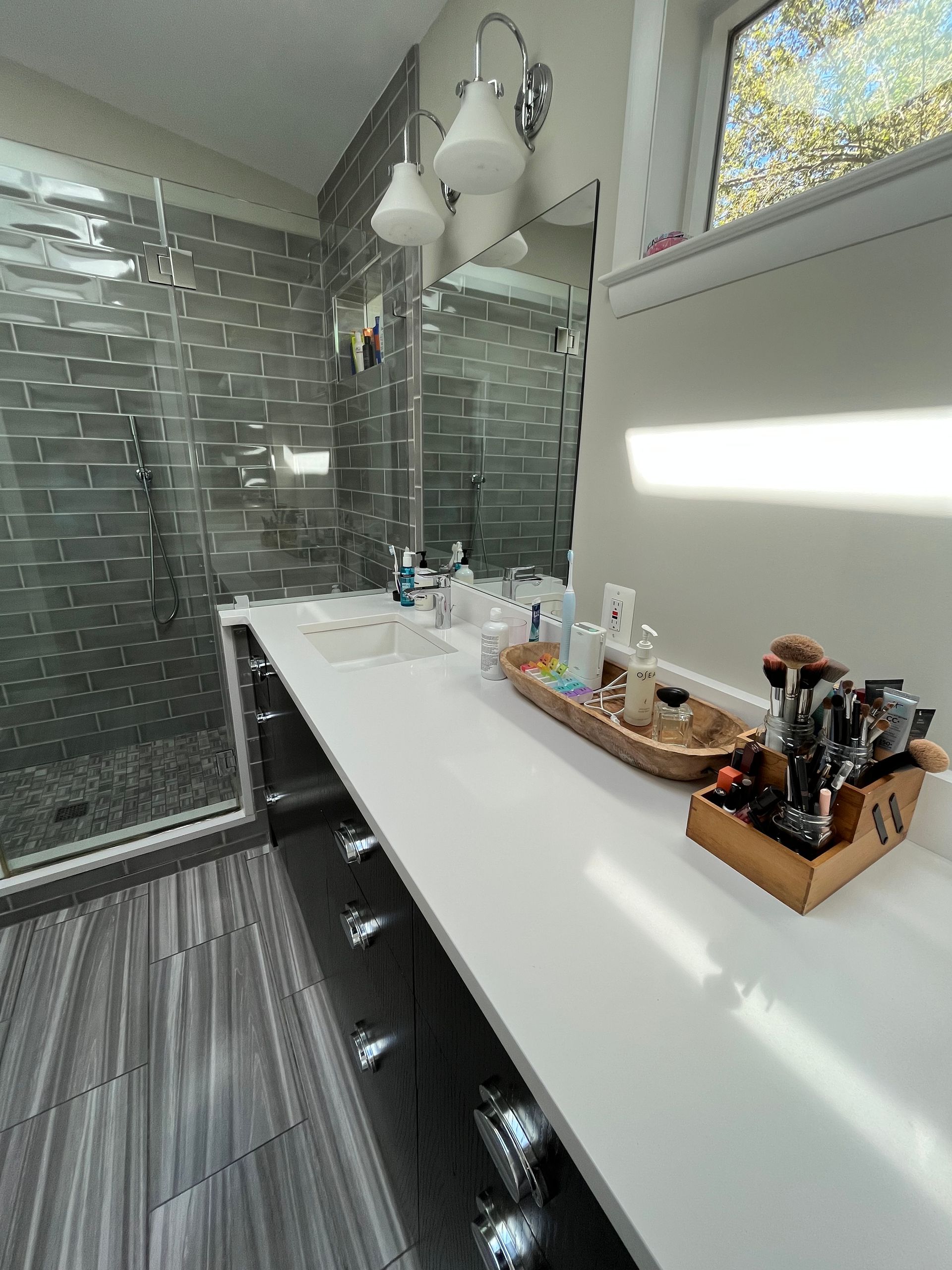 Bathroom with gray tile, white countertop, mirror, and decorative items.