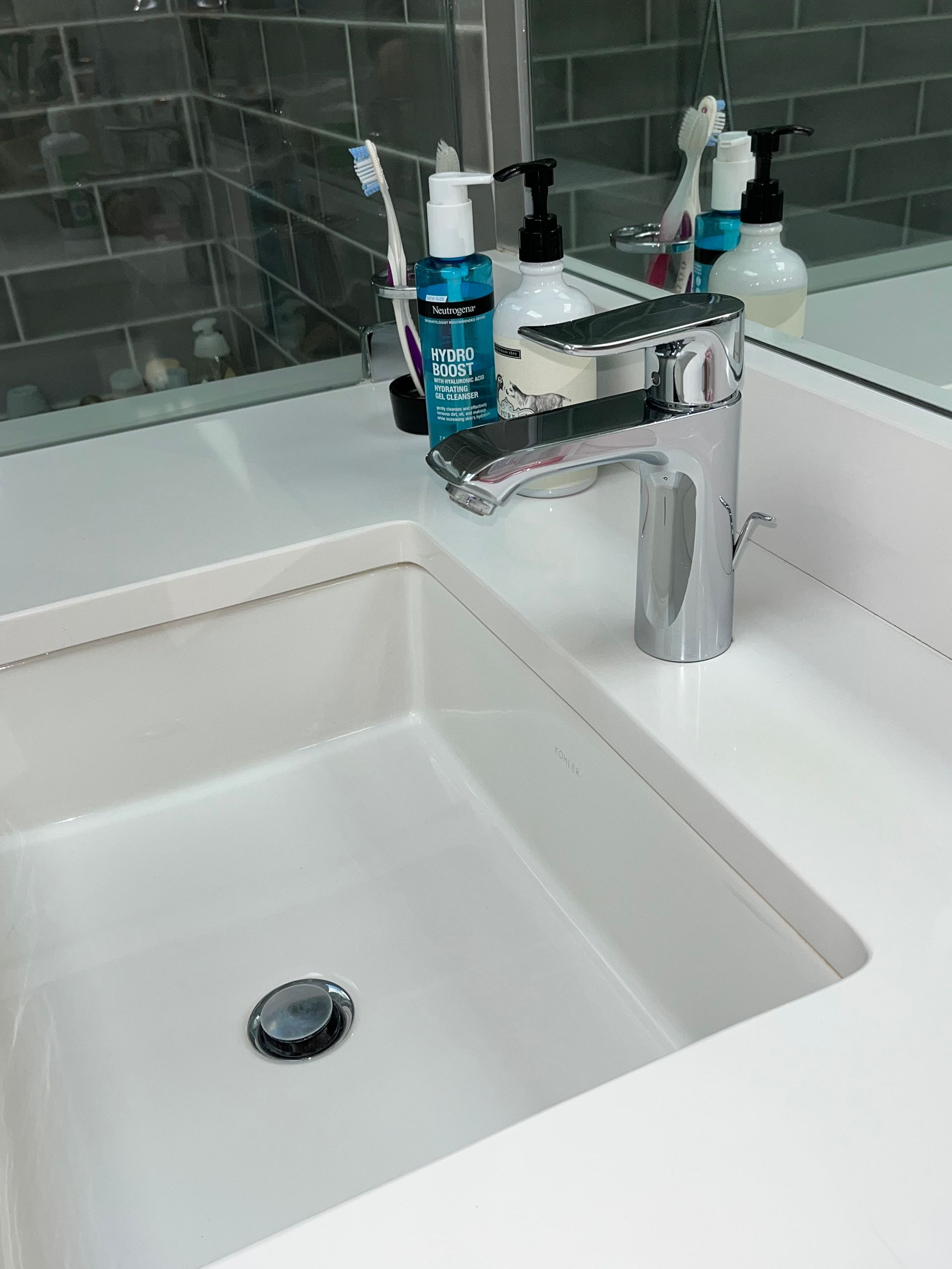 White bathroom sink with chrome faucet, toiletries, and mirror.