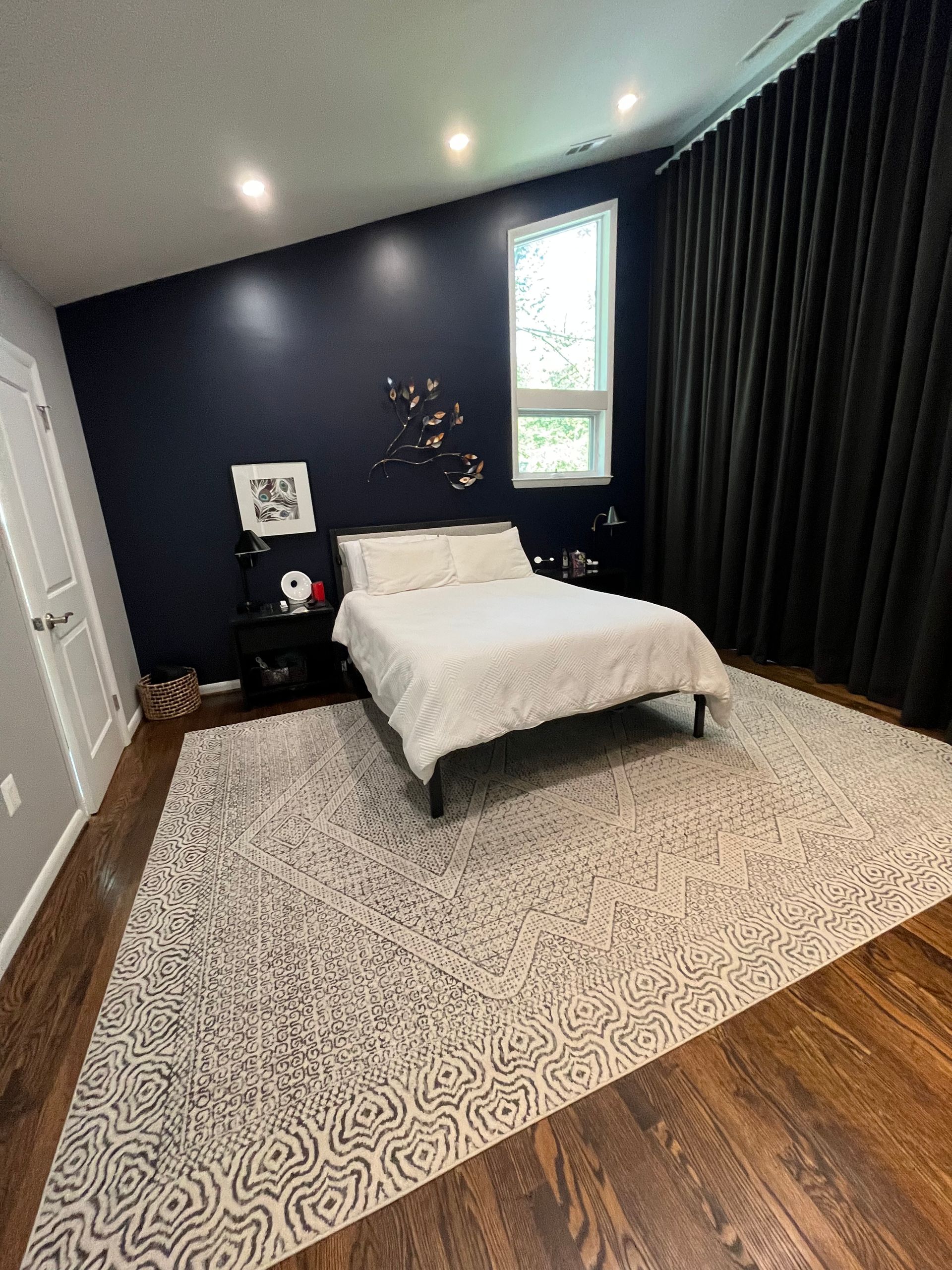 Bedroom with dark blue walls, white bed, large patterned rug, and dark curtains.