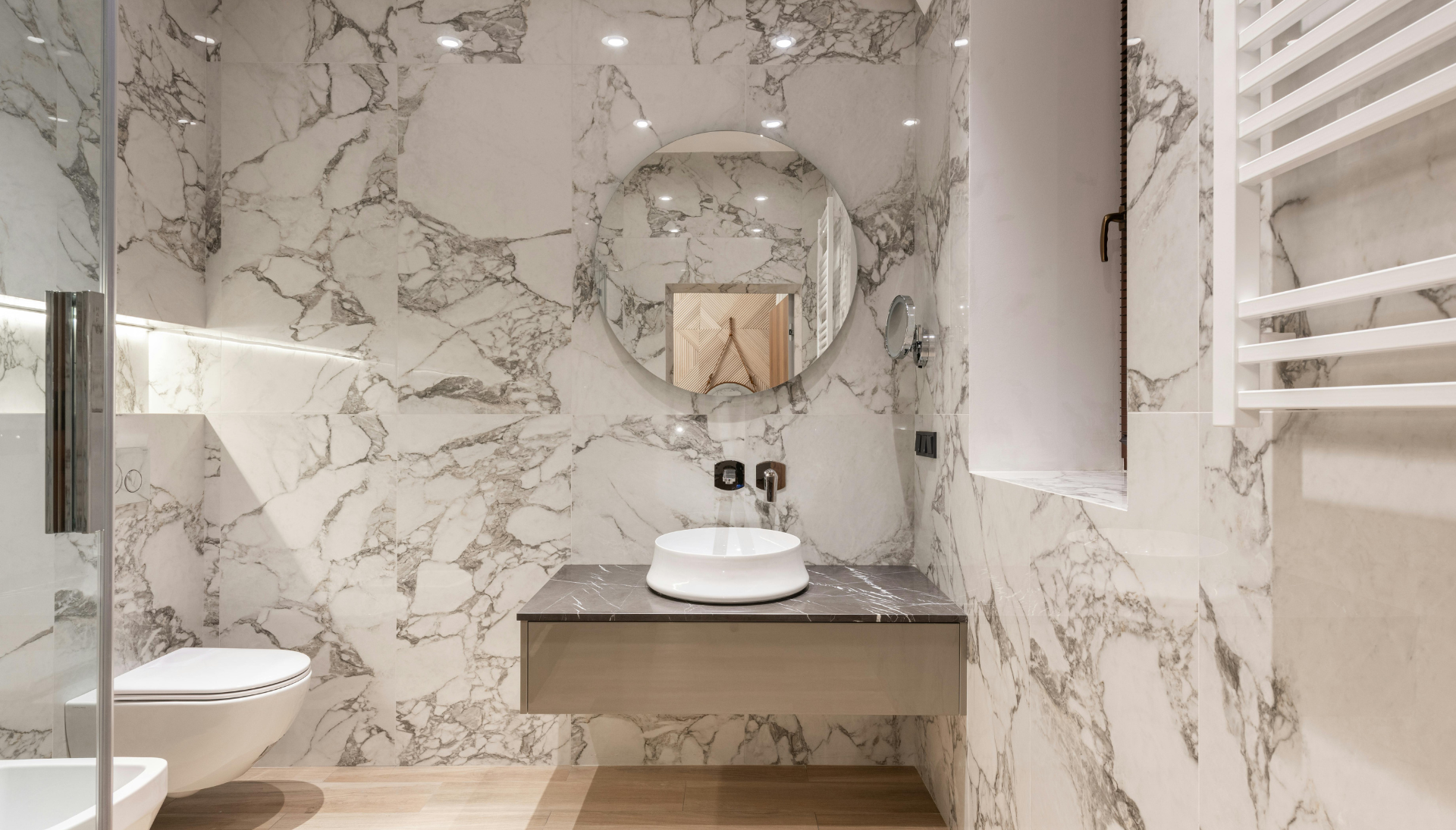 A bathroom with marble walls , a sink , toilet and shower.