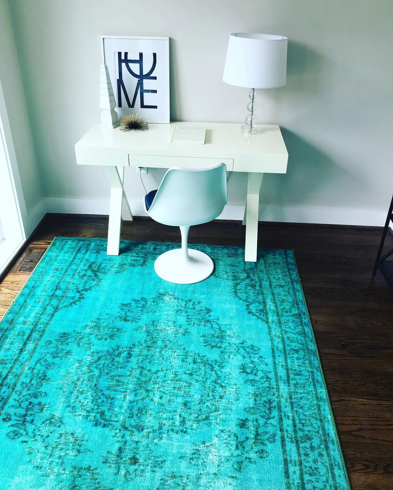 A white desk with a white chair and a turquoise rug in front of it.
