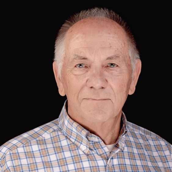 A man in a plaid shirt is standing in front of a black background.