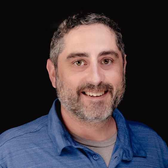 A man with a beard is wearing a blue shirt and smiling.