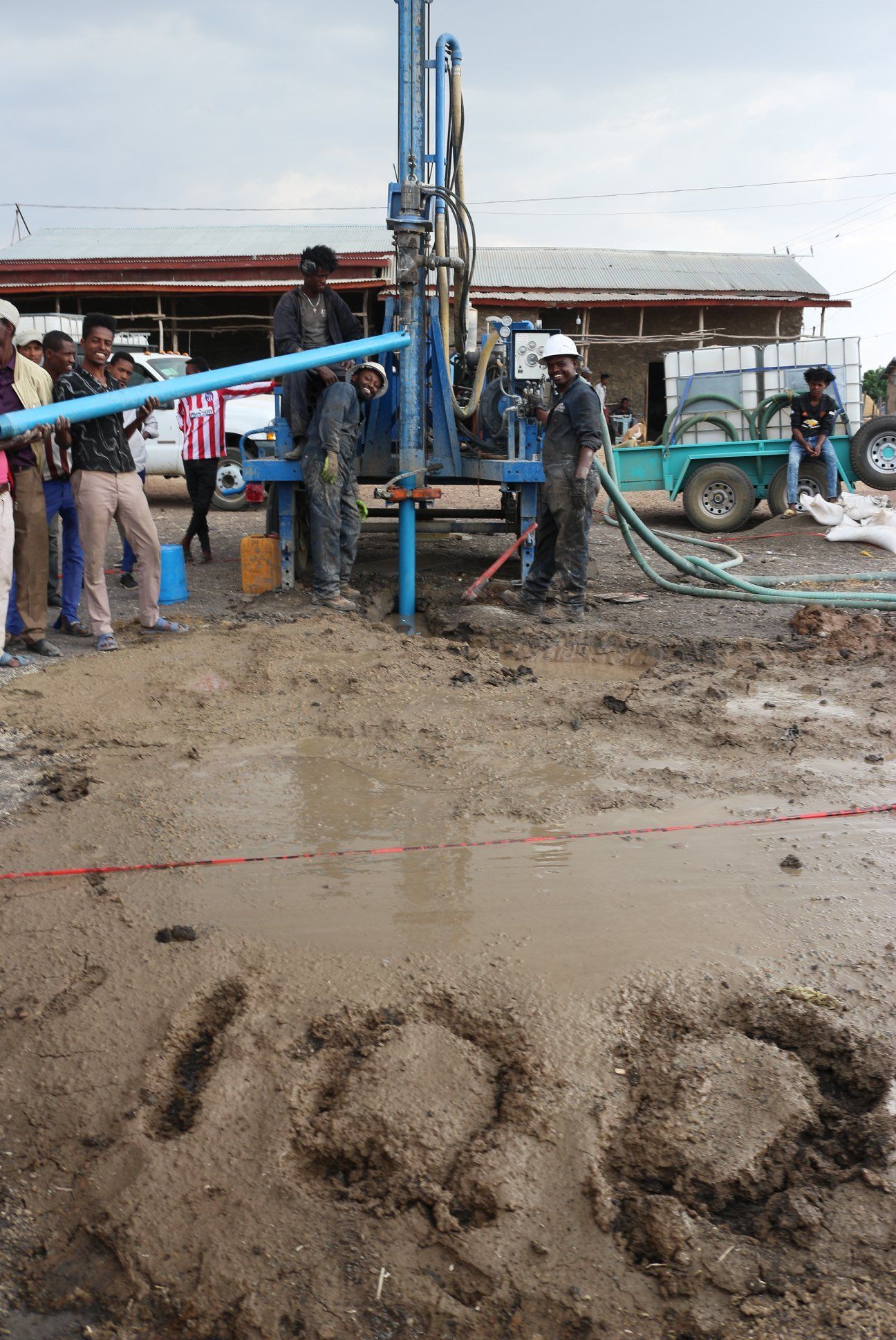 A group of people are standing around a muddy area with the number 100 written in the dirt