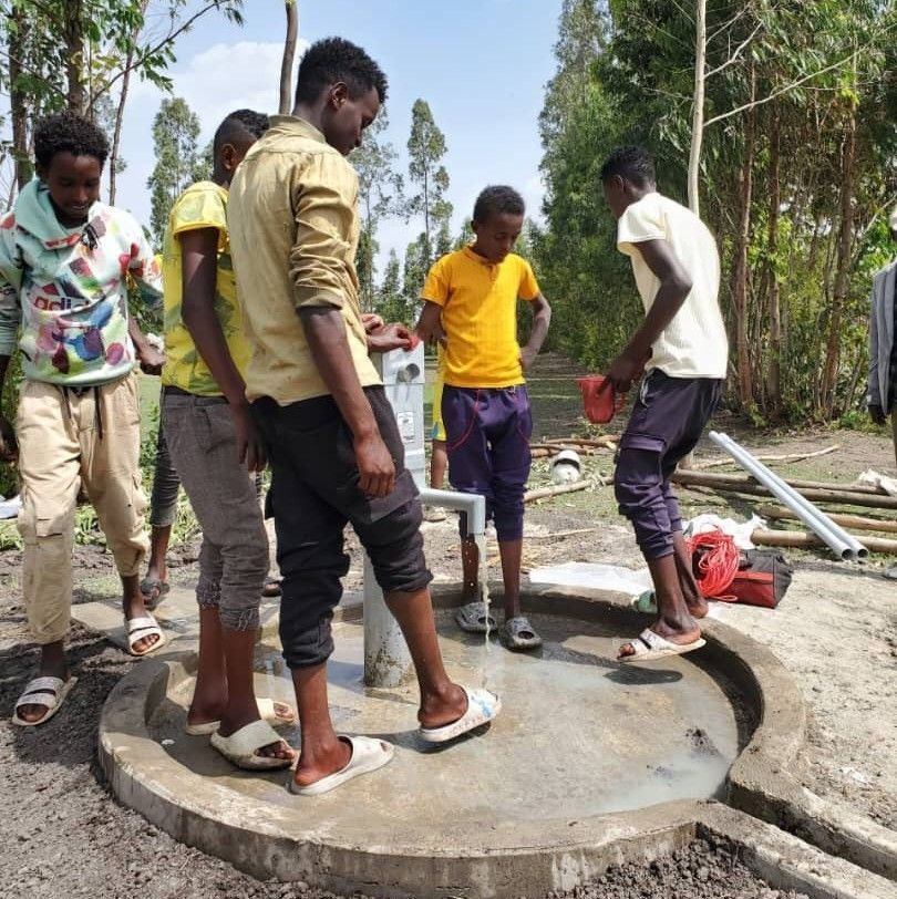 A group of boys standing around a new well.