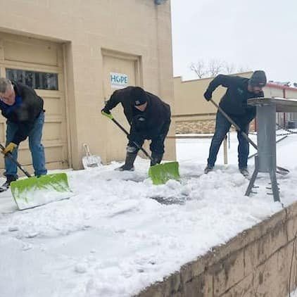 Three men are shoveling snow in front of a building.