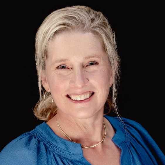 A woman wearing a blue shirt and a necklace is smiling for the camera.