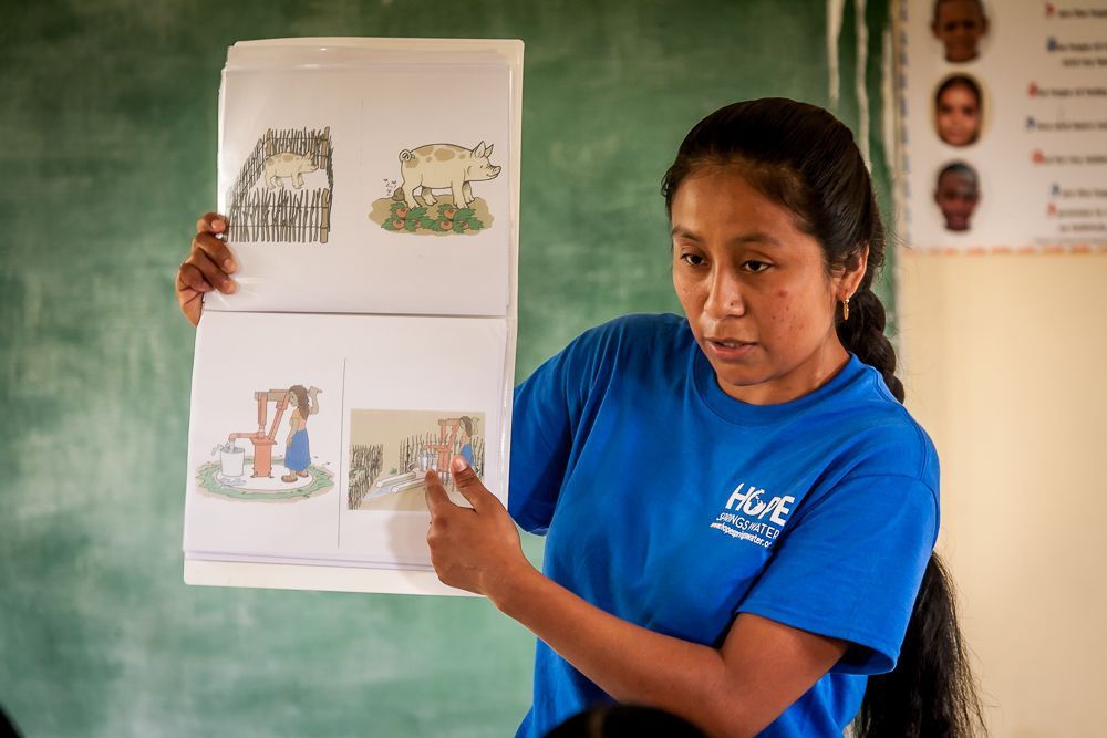 A woman in a blue shirt is holding a book with pictures on it.