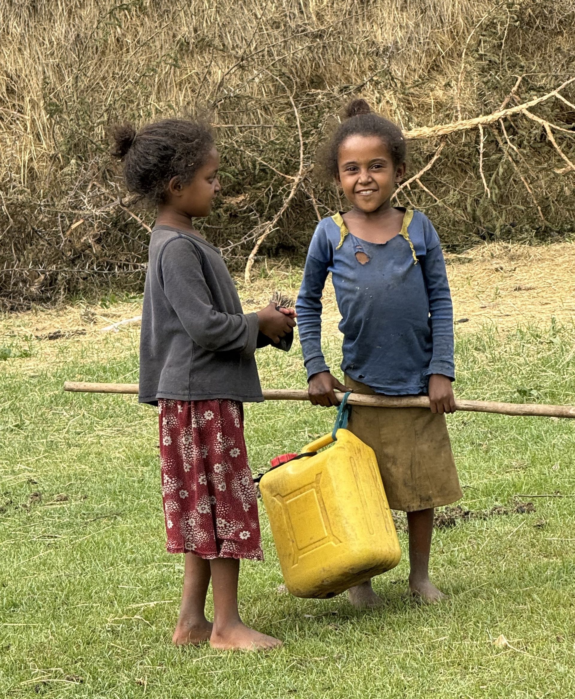 Two young girls are standing next to each other in a grassy field.