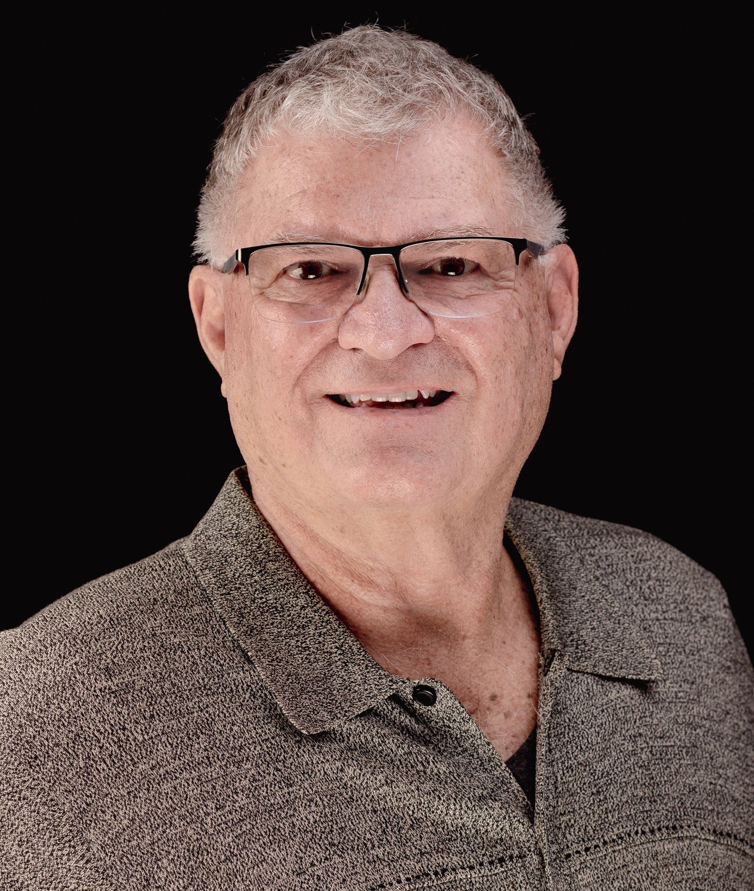 A man wearing glasses and a shirt is smiling for the camera.