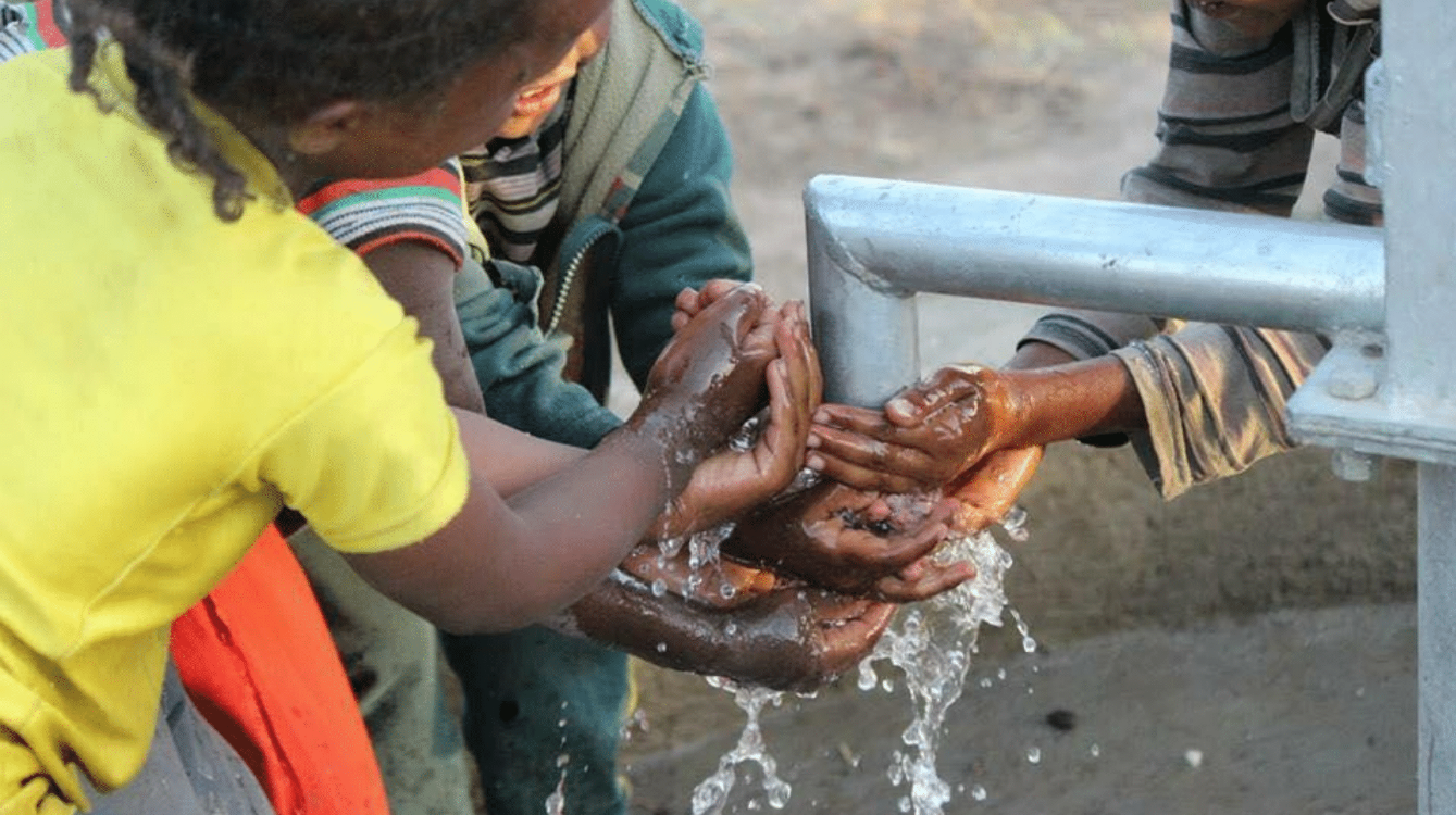 A group of children are washing their hands at a water pump.