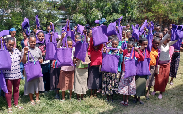 A classroom full of girls are holding up their MHM kits.