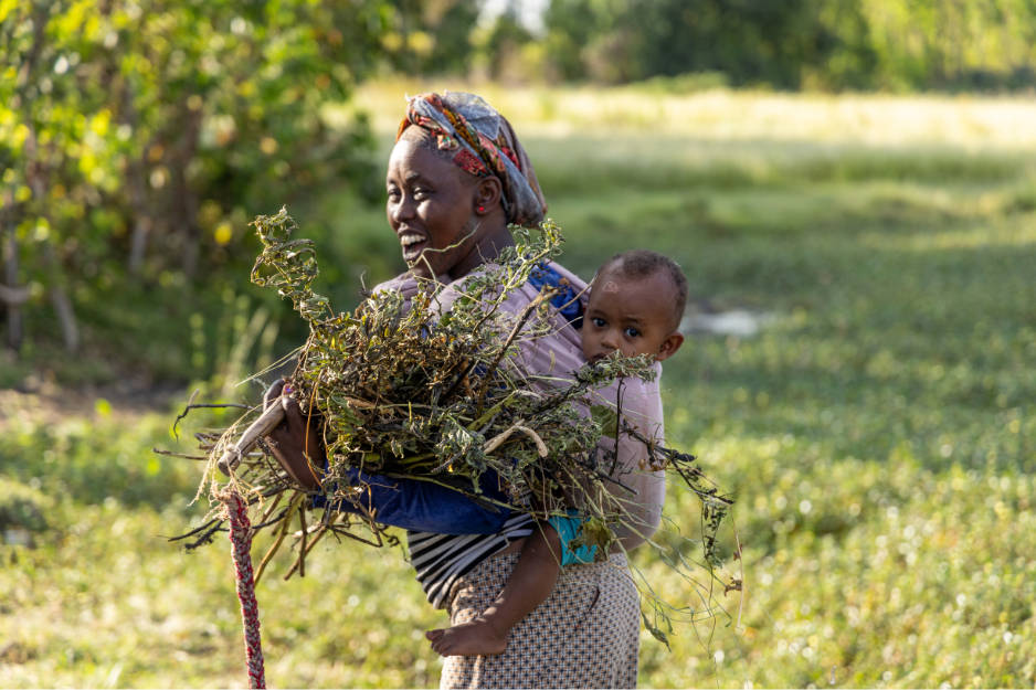 A woman is carrying a baby on her back in a field.