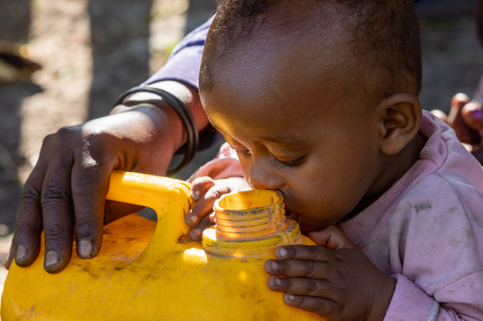 A baby is drinking water from a yellow container.