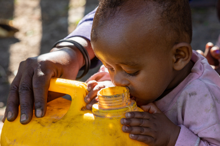 A baby is drinking water from a yellow container.
