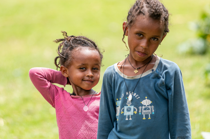 Two little girls are standing next to each other in the grass.
