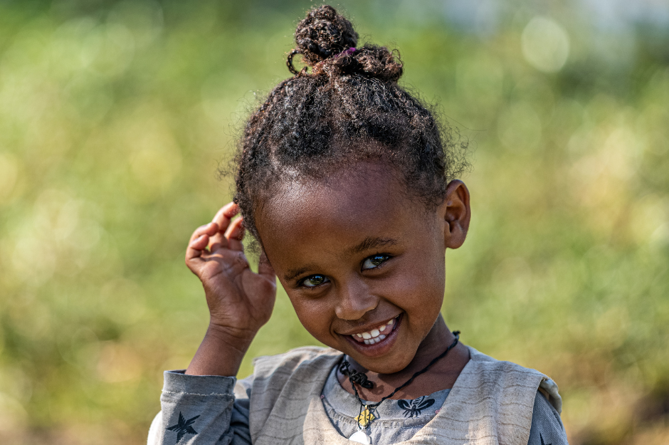 A little girl is smiling and touching her hair.