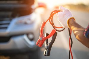 A person is holding a pair of jumper cables in front of a car.