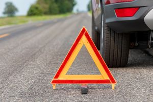 A warning triangle is sitting on the side of the road next to a car.