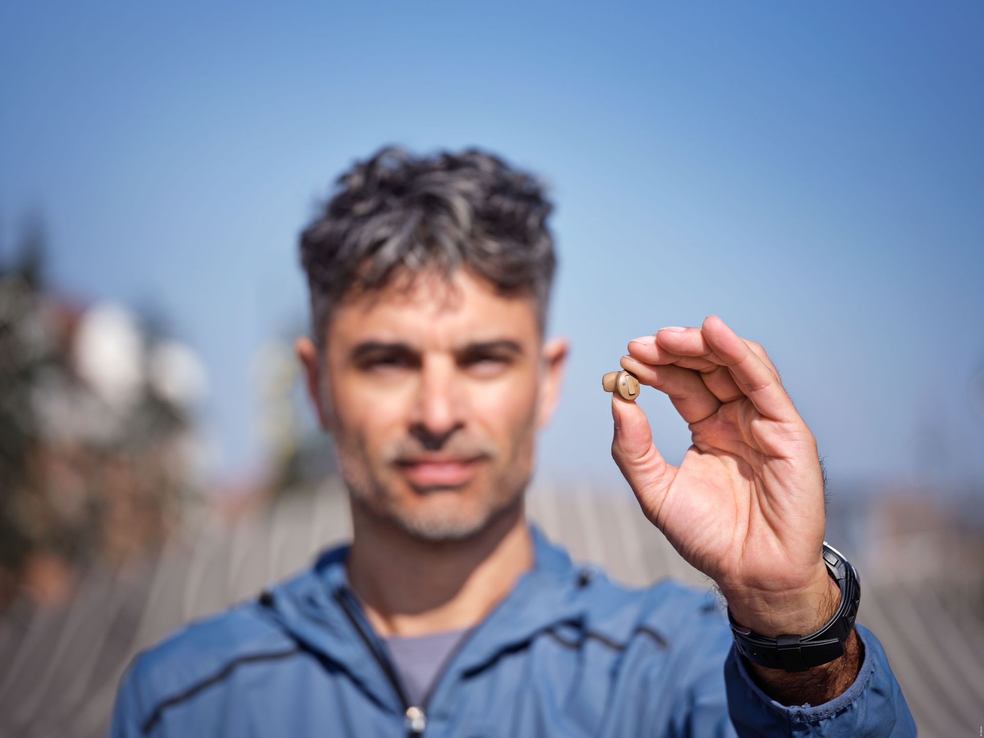 Maður heldur á litlum hlut utandyra, blár himinn í bakgrunni.