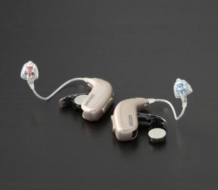 Tvö ljósbrún heyrnartæki með gegnsæjum slöngum, svörtu yfirborði.