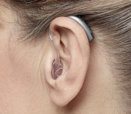 Eyra einstaklings með heyrnartæki sem er sett á bak við eyrað, tengt með gegnsæju röri við eyrnagöngin.