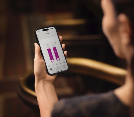 Maður heldur á snjallsíma sem sýnir app með tveimur bleikum súlum og stjórntækjum.