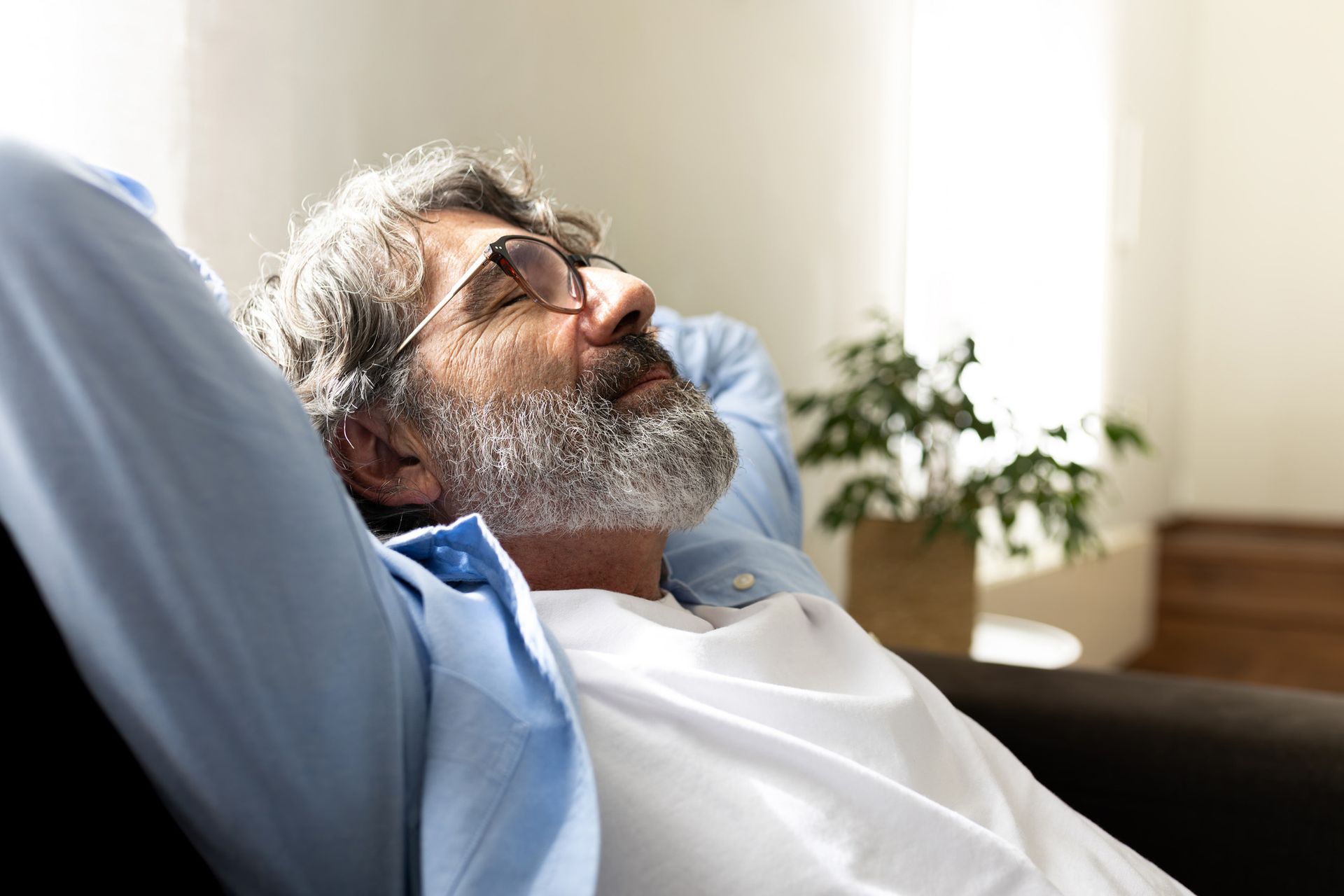 Maður með gleraugu og skegg liggur í sófa, með lokuð augun og hendurnar fyrir aftan höfuð.