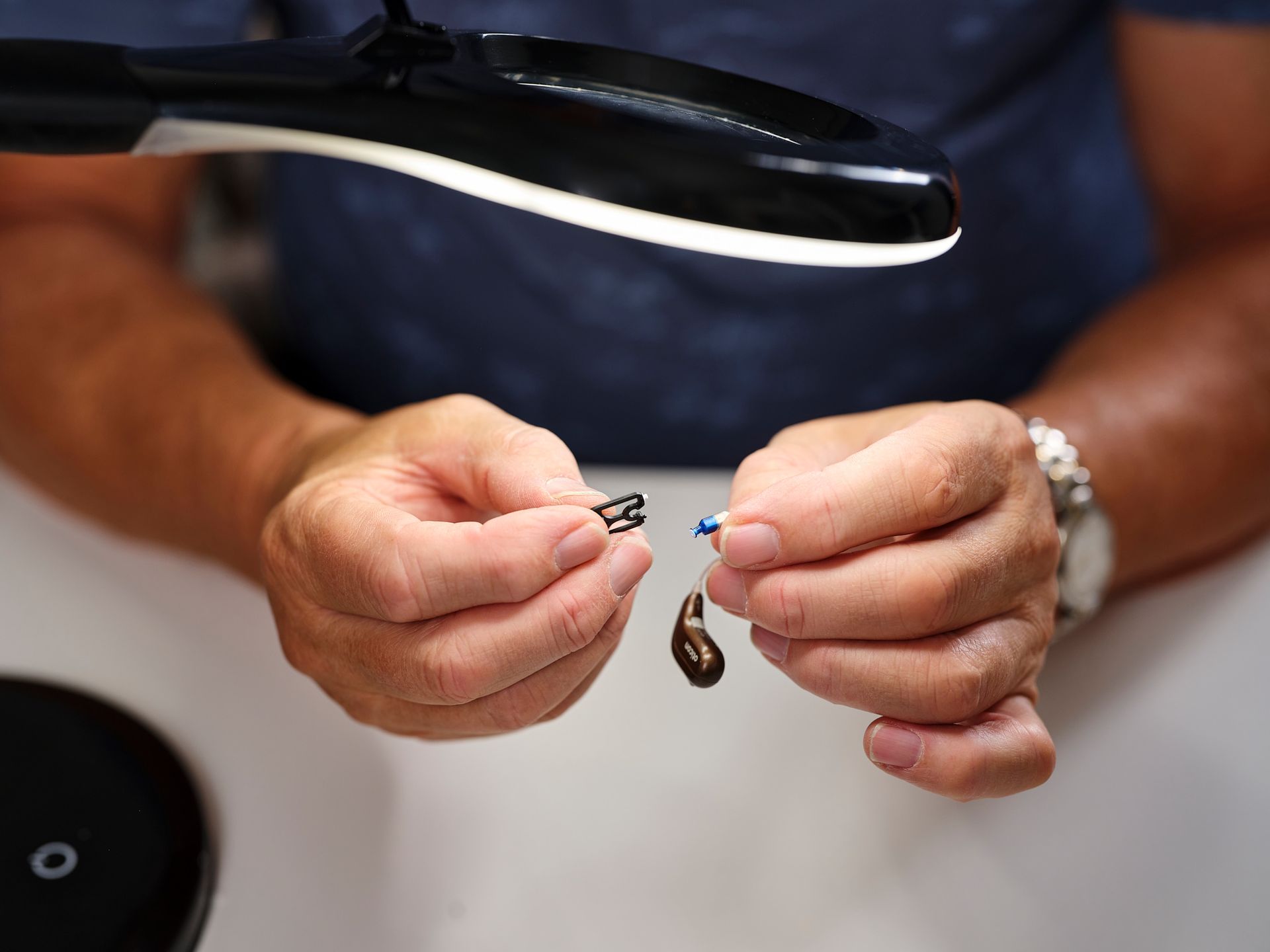 Hendur halda á litlum skartgripum undir skrifborðslampa.