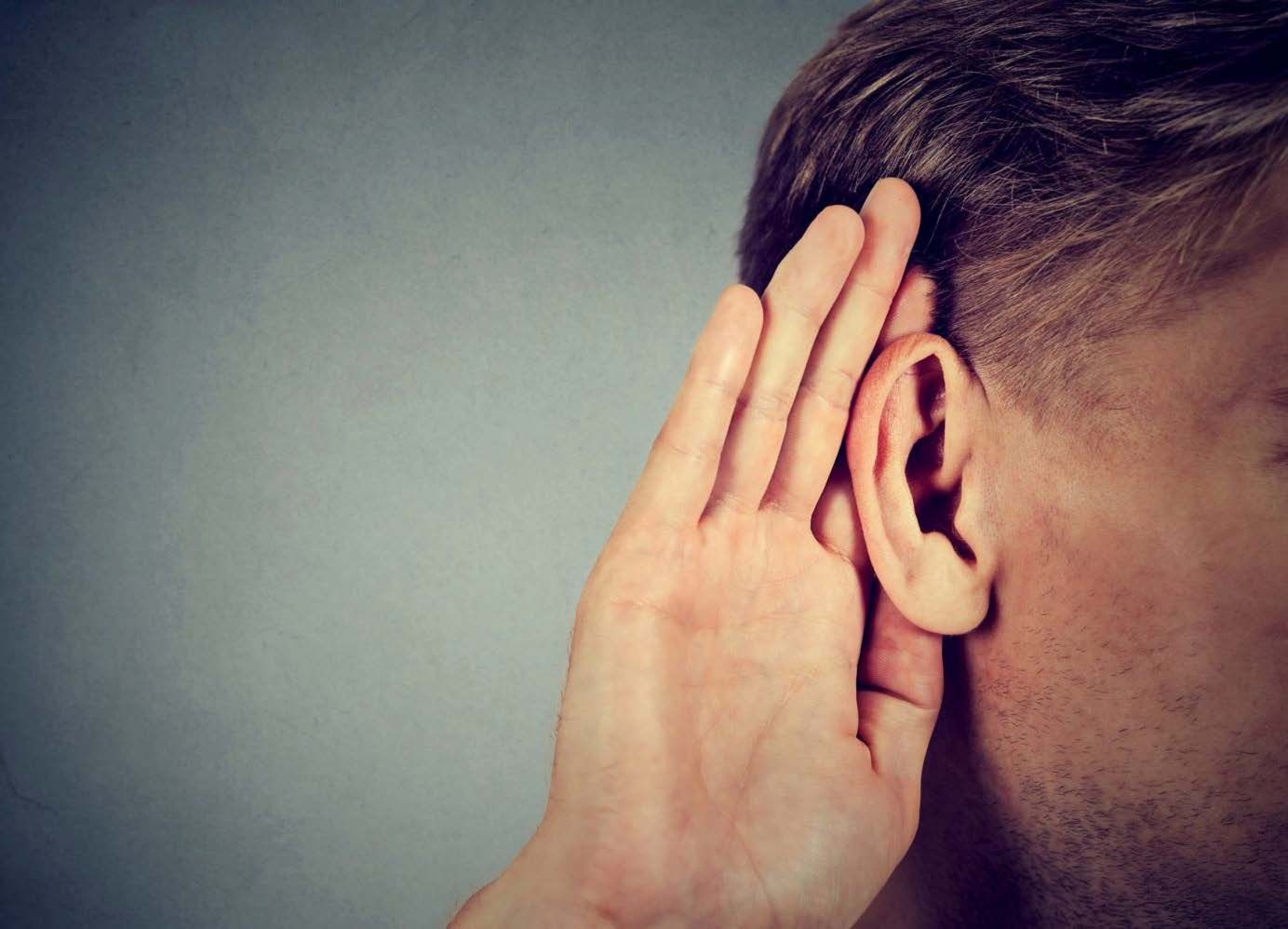 Maður með höndina á bak við eyrað, hlustar af athygli.