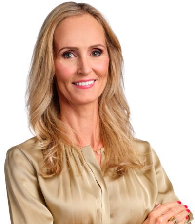 Kona með ljóst hár í gullinni blússu, brosandi, með krosslagða hendur.