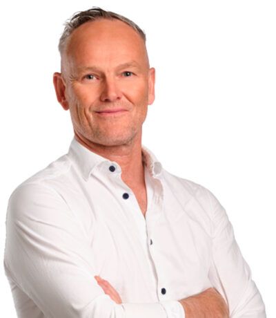 Maður í hvítum skyrtu með krosslagða hendur, brosandi.