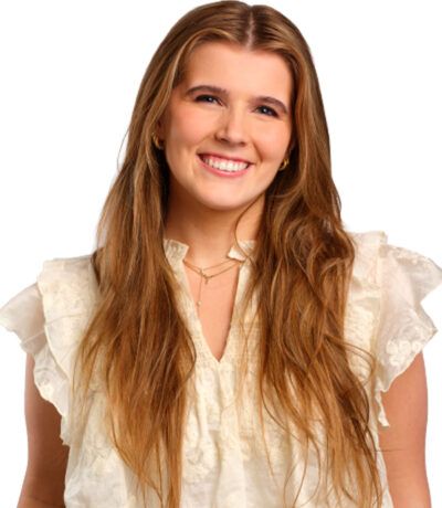 Kona með sítt, ljósbrúnt hár brosir, klædd í hvítan topp með blúnduermum og fíngerðu hálsmen.