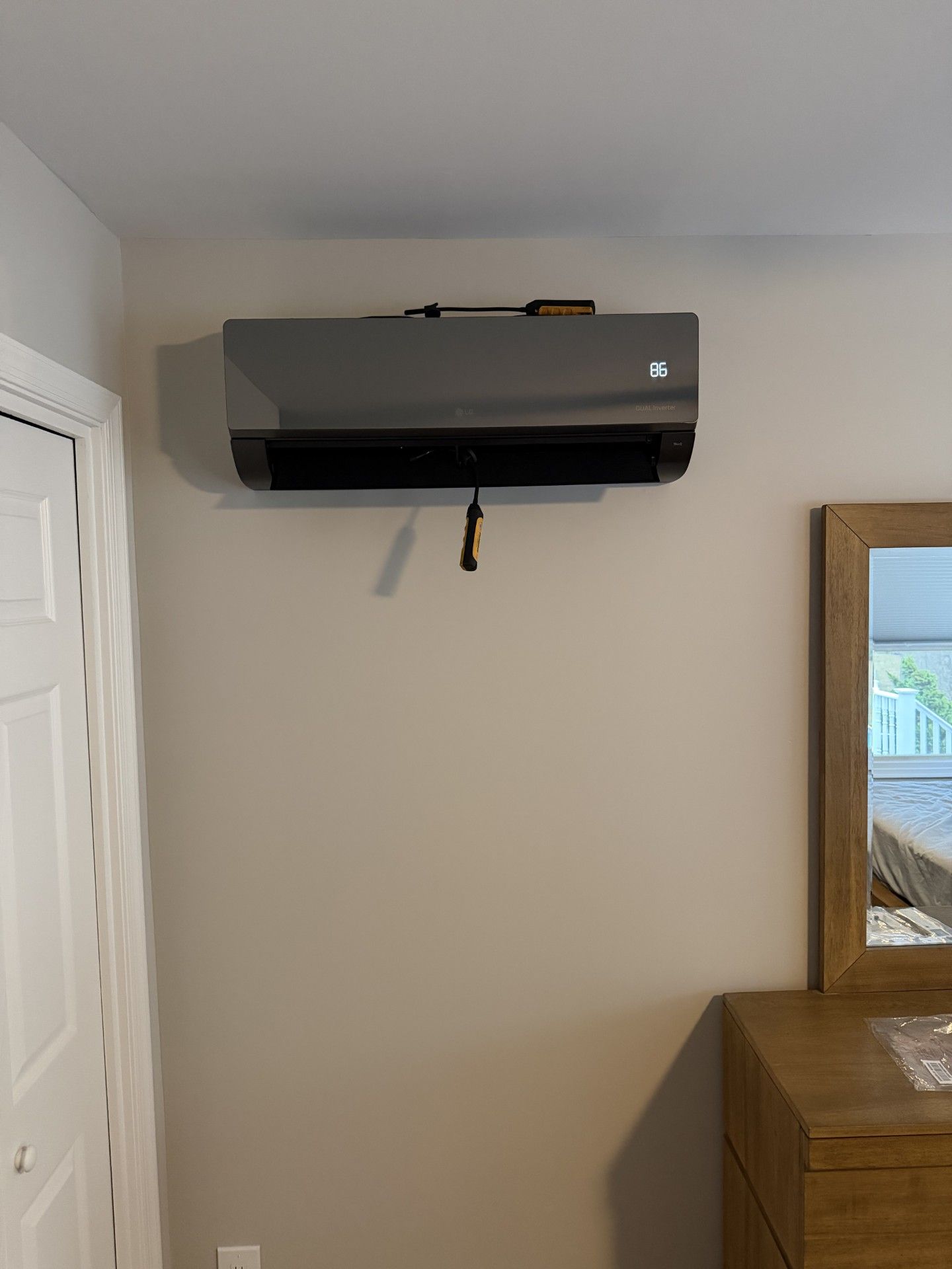 Hands wearing blue gloves hold a small, white portable air cooler in front of a wall-mounted AC unit.