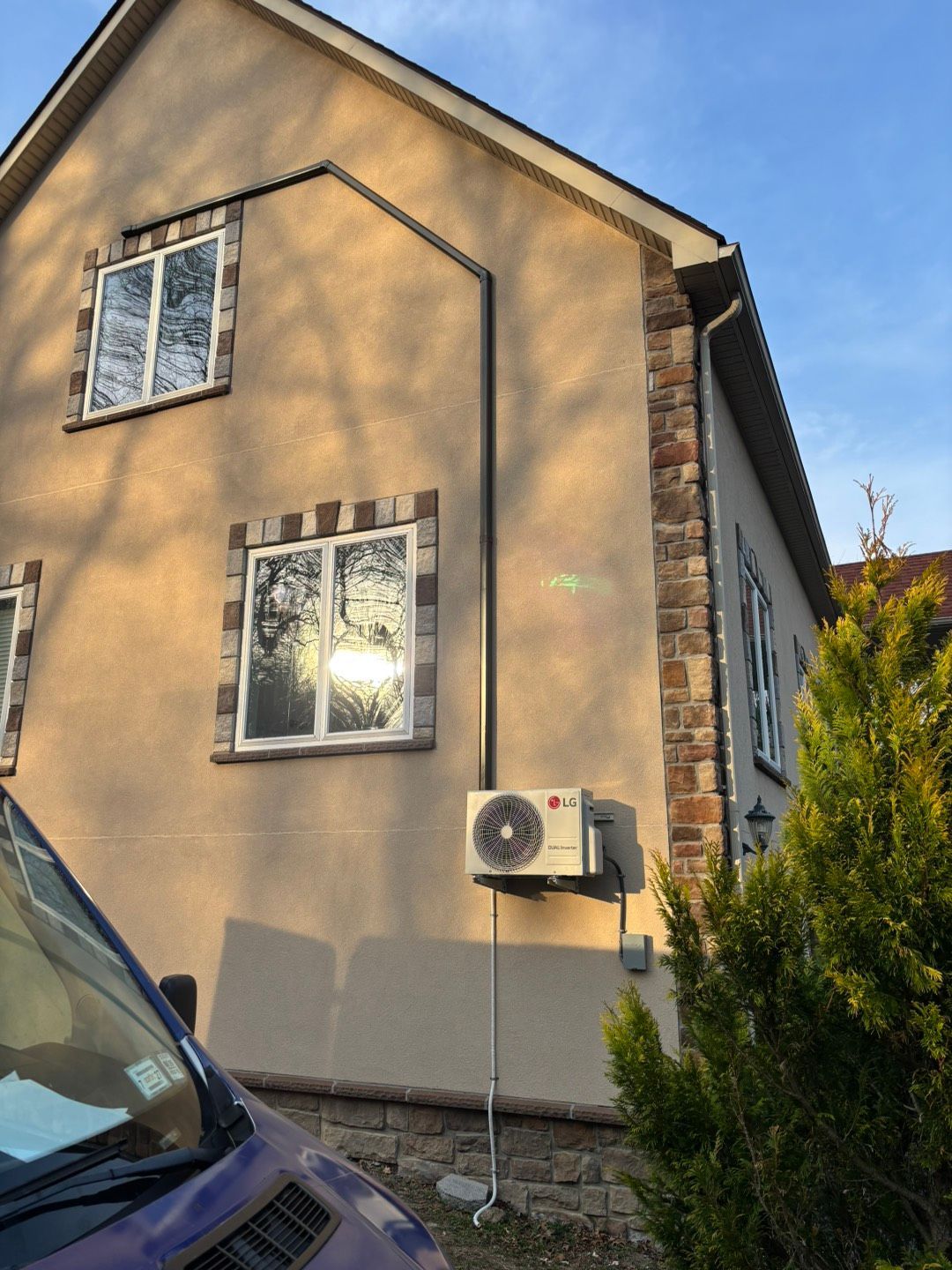 A technician in a grey work jacket installs or services a white air conditioner unit mounted on a wall in a kitchen.