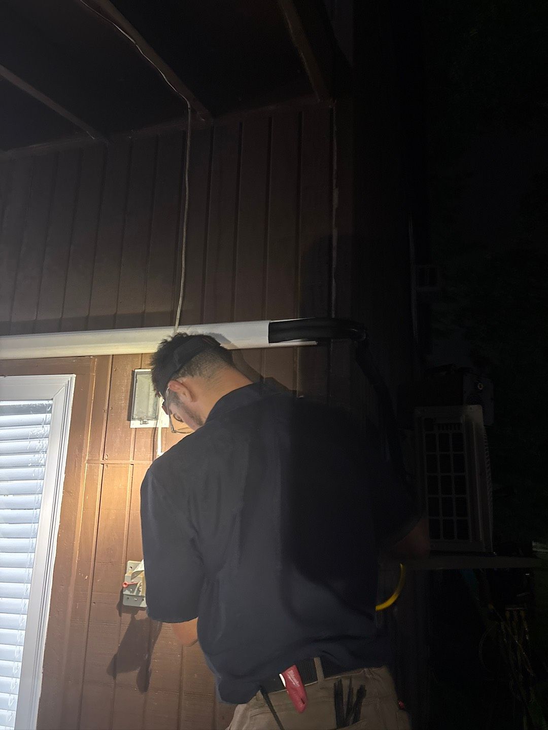 A technician in dark clothing and gloves inspects an outdoor industrial HVAC unit while holding a clipboard.