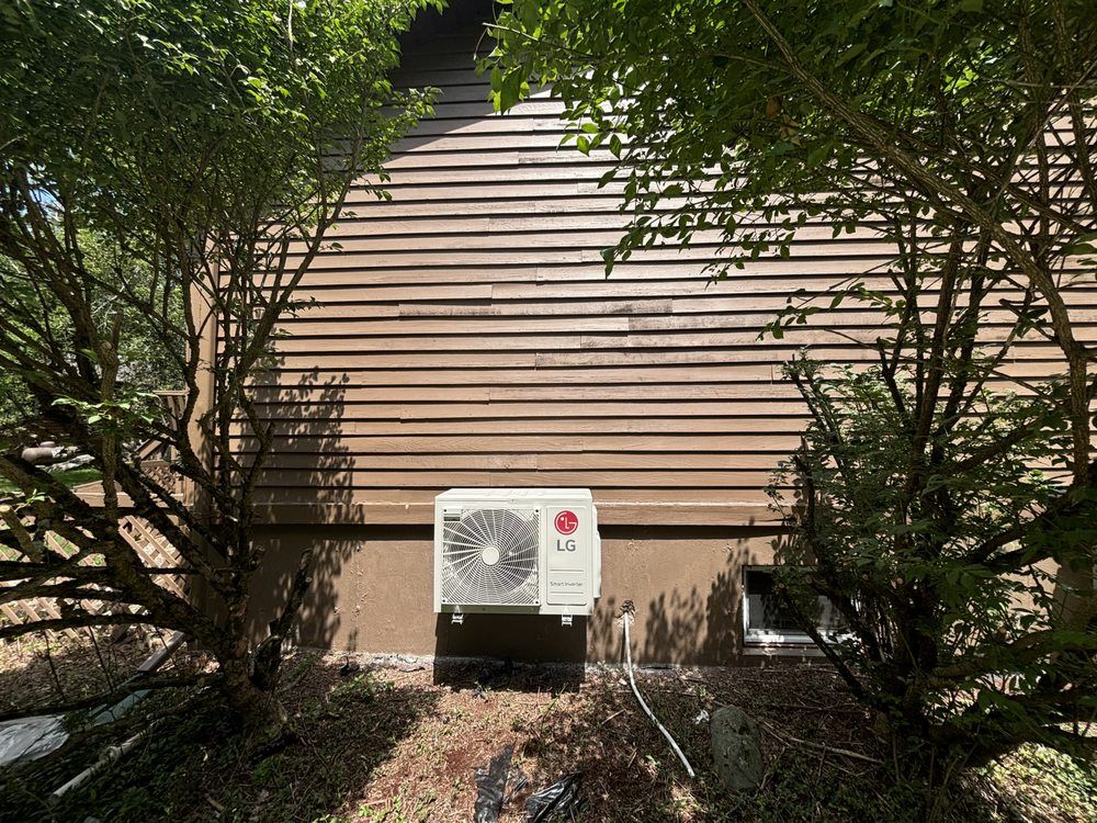 Two grey outdoor air conditioning units on concrete pads next to a house wall and stone retaining wall.