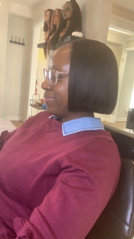 Woman with a smooth, dark bob hairstyle wearing glasses and a maroon shirt, in a salon.