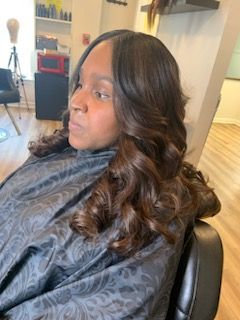Woman with dark, wavy hair, styled with layers, in a salon chair, wearing a black cape.