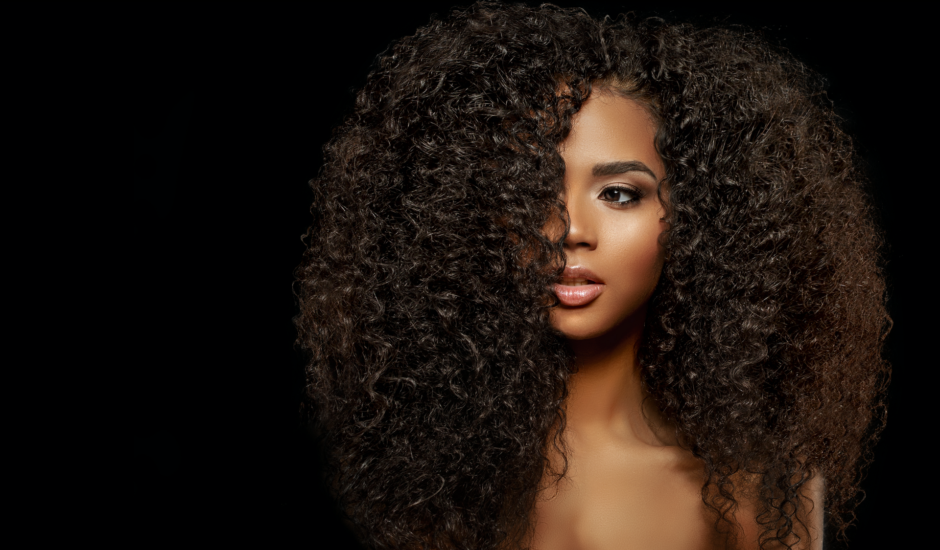 Woman with dark curly hair against a black background.