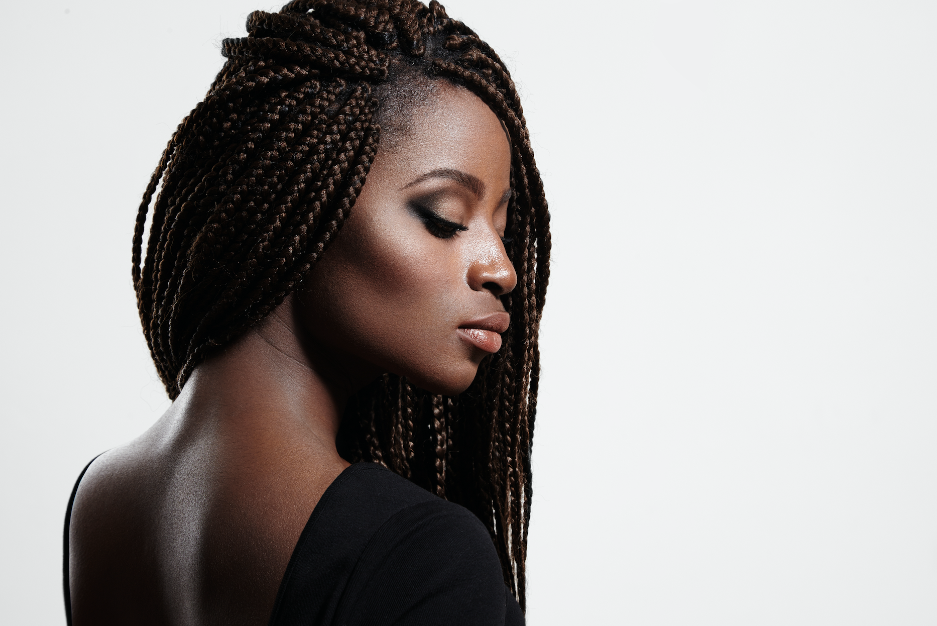 Woman with braided hair, eyes closed, wearing a black top against a white background.