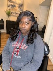 Woman in a grey hoodie with a South Carolina sweatshirt, styled hair. Seated in a chair.