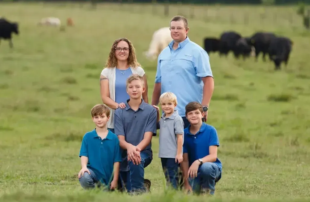 Family of six poses in a green field with cows in the background.
