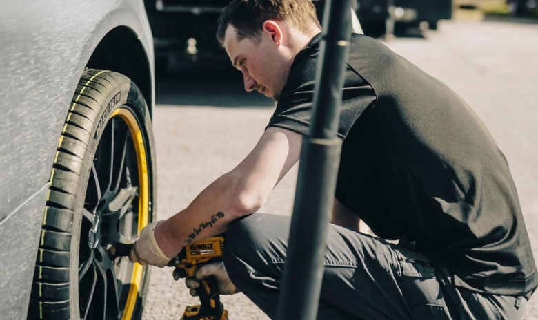 Person crouching beside a car, tightening a wheel with a tool. | Hangar Unlimited Auto Care & Tires